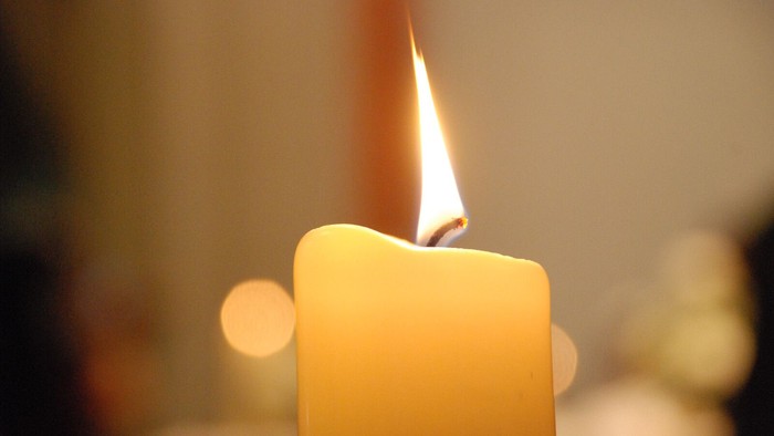 Kerze mit Flamme, heller unscharfer Hintergrund.