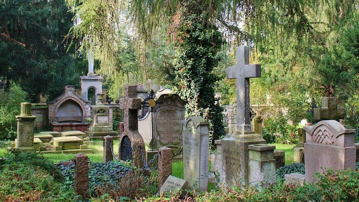 Ein alter Friedhof mit verwitterten Grabsteinen und einem großen Baum.