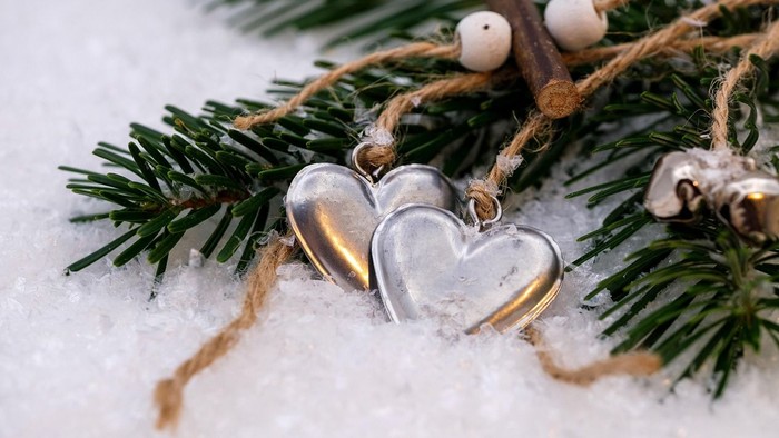 Zwei silberne Herzanhänger im Schnee mit Tannenzweigen