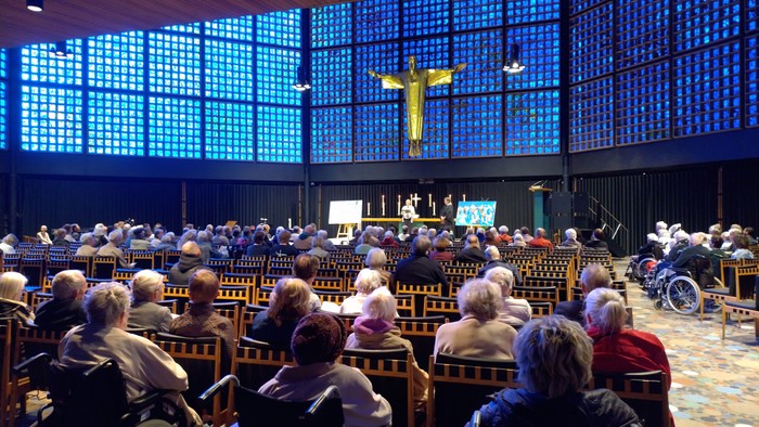 Gottesdienst in einer modernen Kirche mit vielen Gläubigen und einem großen Kreuz im Hintergrund