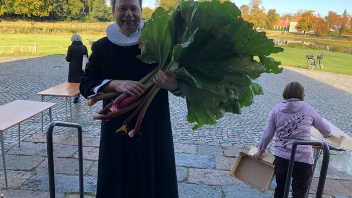 Mand i svart kappe holder en stor rhubarbbund.