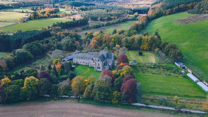 Eine Klosteranlage aus grauem Stein liegt inmitten einer Herbstlandschaft.