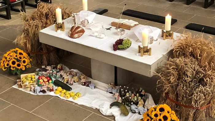 Ein Tisch mit Kerzen, Blumen und verschiedenen Gegenständen, umgeben von Strohballen und weiteren Blumenarrangements