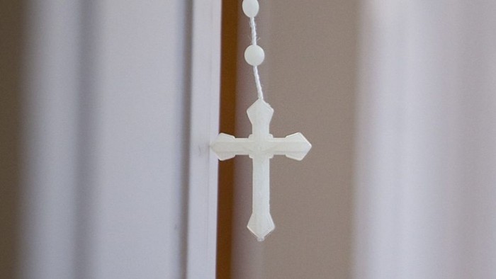 Ein weißes Kreuz hängt an einer Perlenkette an einer Tür.