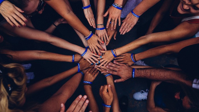 People with blue wristbands joining hands in a circle.