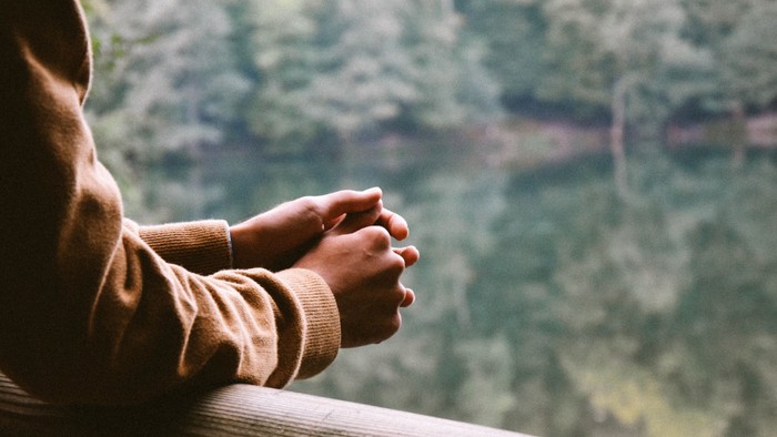 Person sitzt nachdenklich am Fenster und schaut in den Wald.
