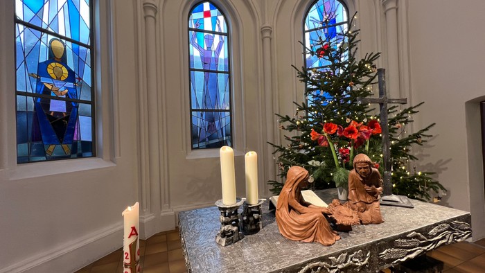 Gepflegte Kirchenbank mit Adventskranz und Weihnachtsbaum vor buntem Fenster