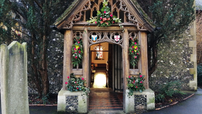 Wooden lych gate with flowers leading to a stone path.