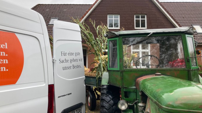 Ein weißer Van und ein grüner Traktor vor einem Haus mit einem Schild, das