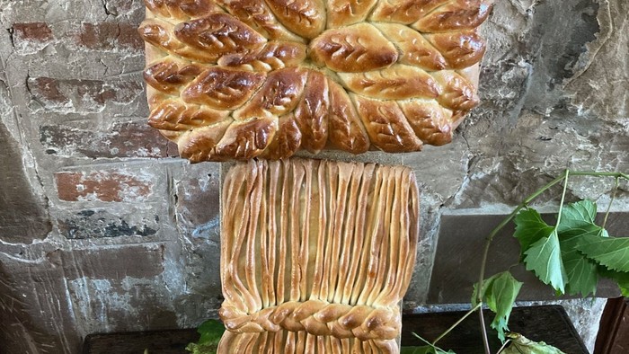 Bread shaped like wheat stalk on stone surface with leaves.