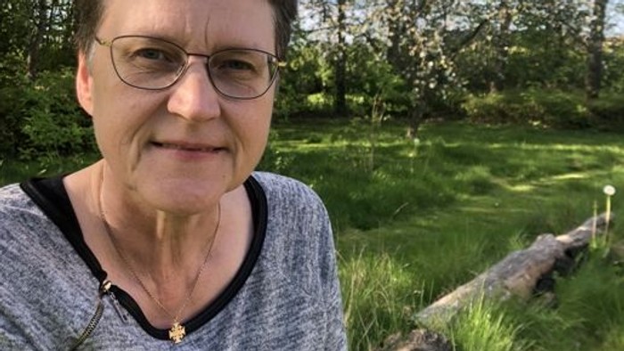 En kvinde sitter udenfor med træer og græs i baggrunden