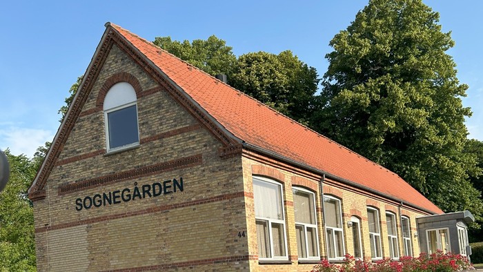 Gamle Sognegård i rød tegl med røde tag og omgivet af grønne træer