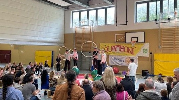 Auf dem Bild sieht man eine Turnhalle. Menschen schauen mehreren Kindern und Jugendlichen bei einer Darbietung mit Gymnastik-Reifen zu.