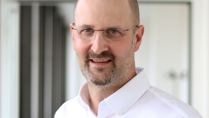 Portraitbild von Markus Specht, ein mittelalter weißer Mann mit Brille und weißen Hemd
