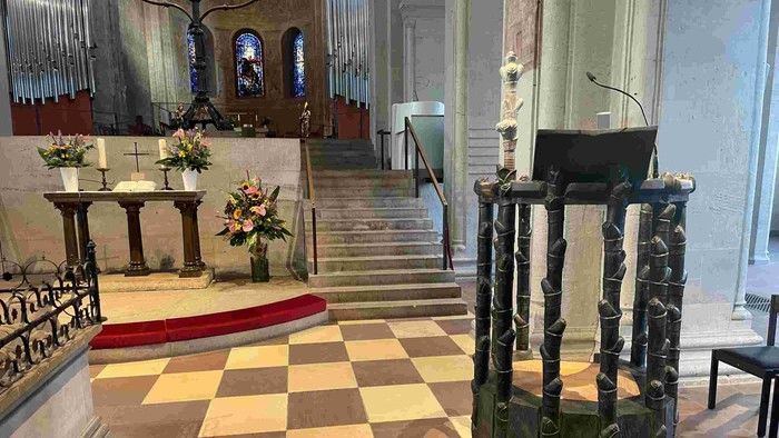 In der Kirche steht ein Pult auf einem Schachbrettboden, umgeben von Blumen und Stufen.