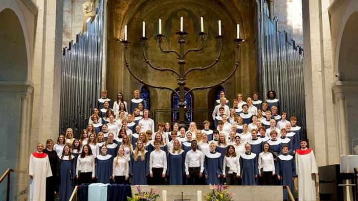 Ein großer Kirchenchor singt vor einem Altar mit Kerzenleuchter