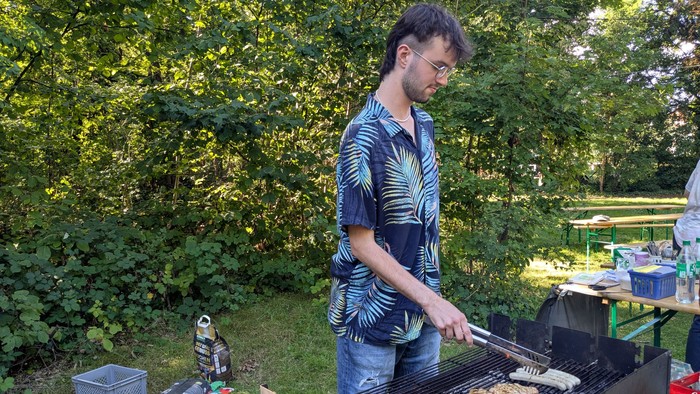 Mann grillt im Freien mit verschiedenen Lebensmitteln und Utensilien um ihn herum