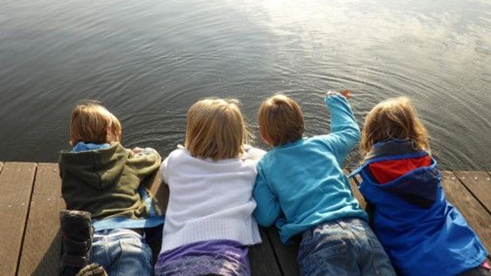 Vier Kinder sitzen auf einer Holzbrücke und schauen ins Wasser