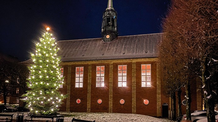 En lysket julesejr ved kirke i snødekt by.