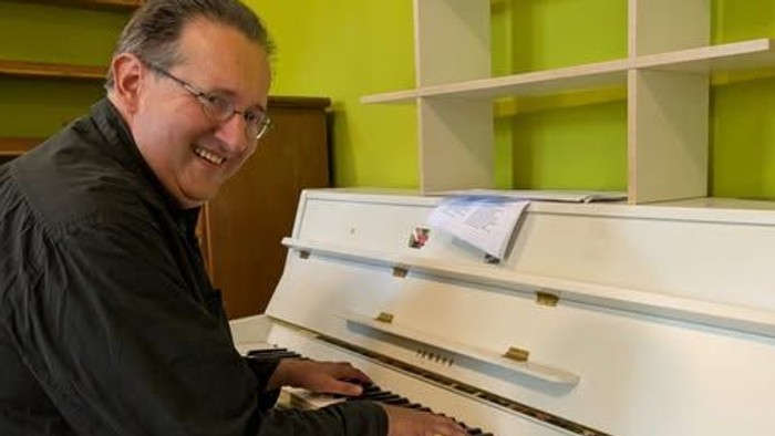 Mann spielt Klavier in einem Raum mit gelben Wänden.