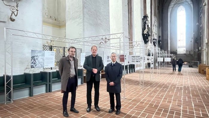 Drei Personen stehen in einer Kirche vor einer Ausstellung.