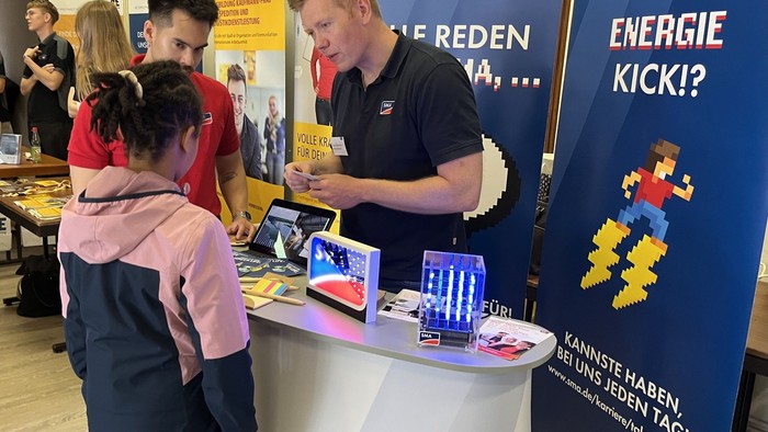 Ein Mann an einem Infostand erklärt zwei Kindern etwas über Energie.