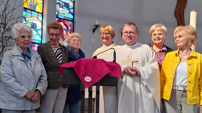 Eine Gruppe von Menschen steht in einer Kirche um einen Mann in weißer Robe, der ein rotes Tuch hält