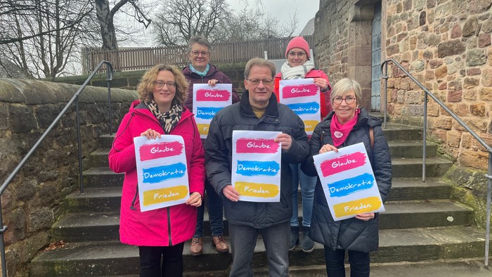 Fünf Personen stehen auf Treppe, halten Plakate mit