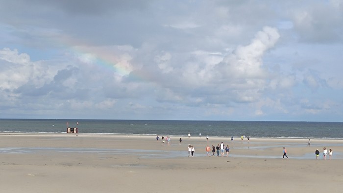 Strand mit Menschen unter bewölktem Himmel und Regenbogen