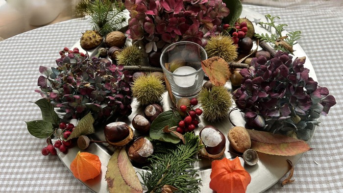 Ein Tablett mit Herbstdekoration, darunter Kastanien, Blumen und Kerze