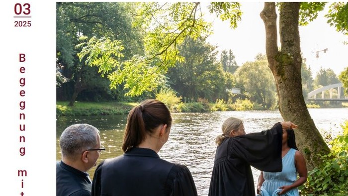 Eine Gruppe von Menschen in Roben steht am Fluss, einer beugt sich vor, um etwas zu berühren