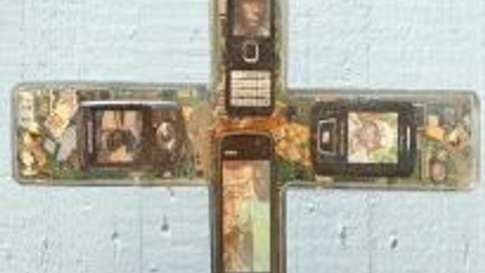 Das Bild zeigt ein Kreuz aus einem veralteten Lineal, an dem kleine Fotos befestigt sind.