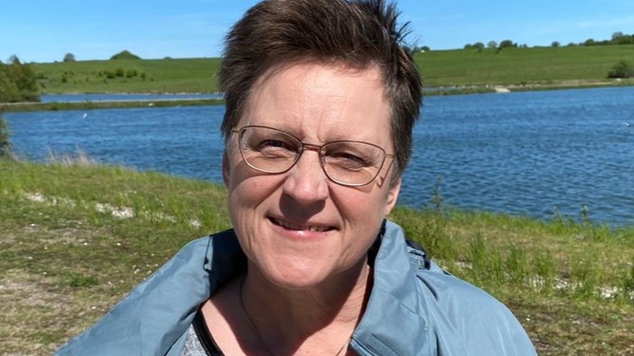 En kvinde står ved en sø og smiler til kameraet