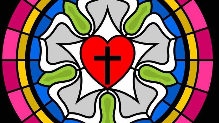 Das Bild zeigt ein buntes Kirchenfenster mit einem roten Herzen und einem Kreuz in der Mitte.