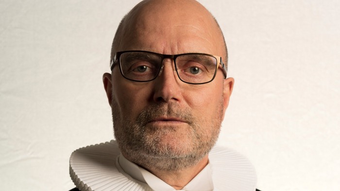 En bald, brillet mand i sort kappe med hvid krage.