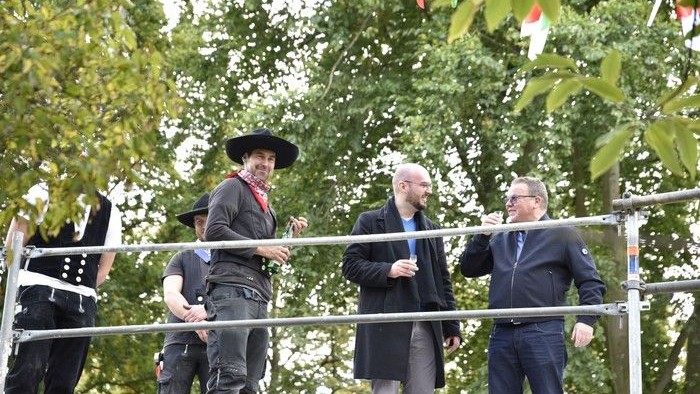 Männer in historischen Kostümen stehen auf einem Podium und unterhalten sich.