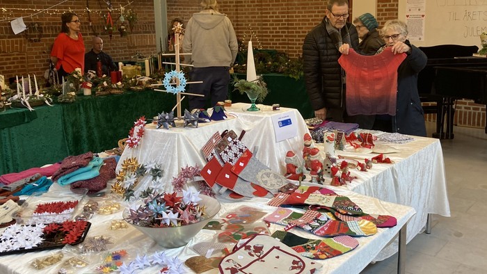 En gruppe mennesker ser på udstillinger på en markedsplads med håndværk og smykker.