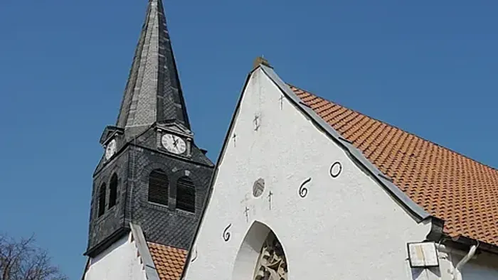 Ansicht der Westseite der Kirche St. Stephan: Zwei Kirchenschiffe nebeneinander mit weißen Wänden, einem schiefergedeckten Turm und der Jahreszahl 1660.
