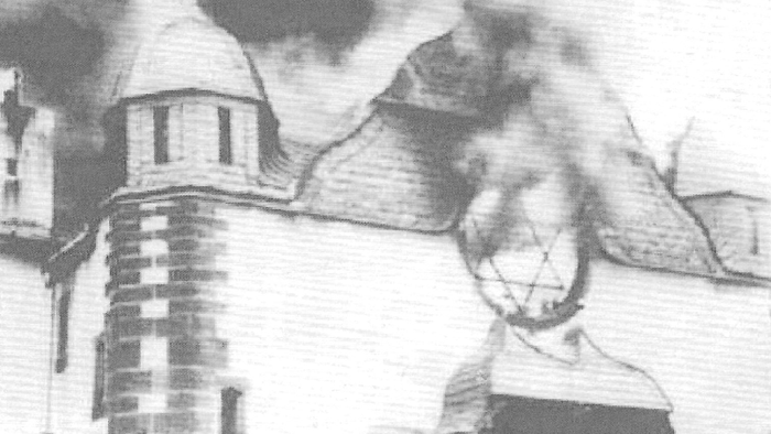 Eine alte Synagoge brennt lichterloh, Rauch steigt auf.