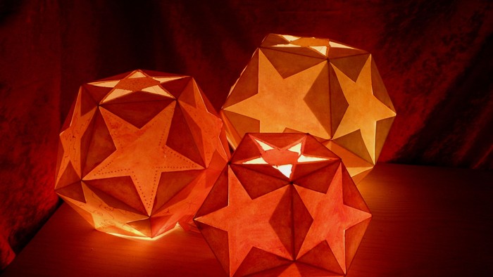 Drei leuchtende Origami-Kugeln in Orange und Gelb auf dunklem Hintergrund