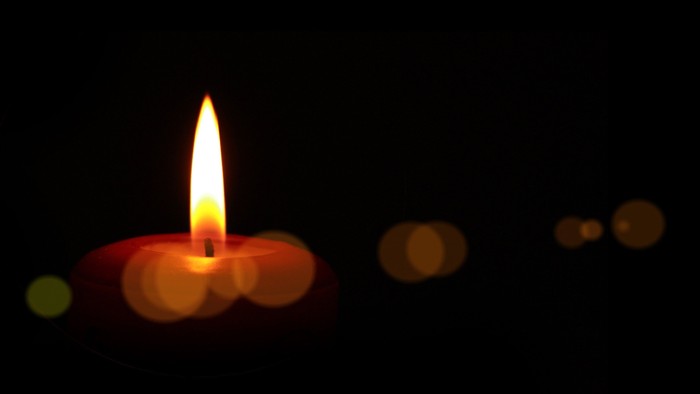 Eine brennende Kerze vor einem dunklen Hintergrund mit Lichtflecken.