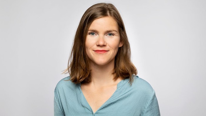 Eine junge Frau mit langen braunen Haaren lächelt in die Kamera.