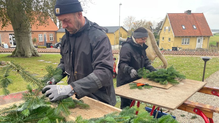 To gravere laver grandekorationer på borde, der er gule huse i baggrunden