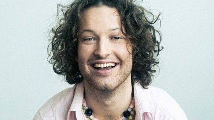 En mand med langt og krøllet hår smiler til kameraet.