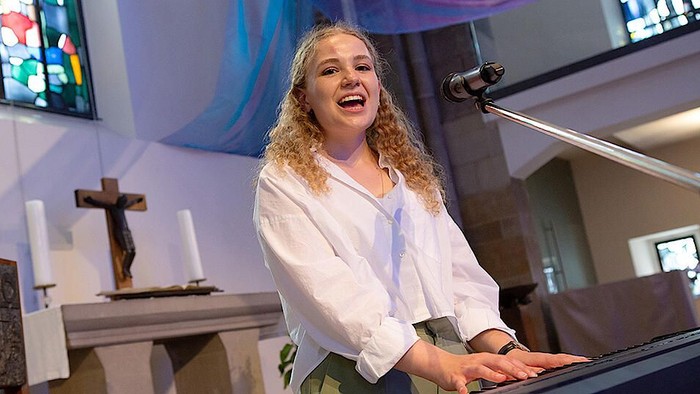 Eine Frau spielt Klavier in einer Kirche und lacht dabei.