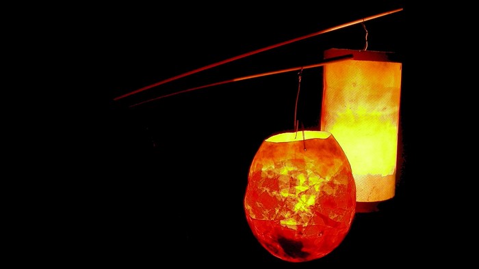 Zwei beleuchtete Laternen hängen an einem Draht, eine rund, die andere zylindrisch