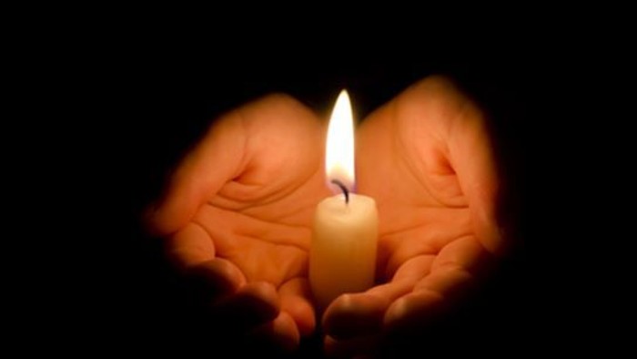 En lysende lyse stået mellem to håndflader.