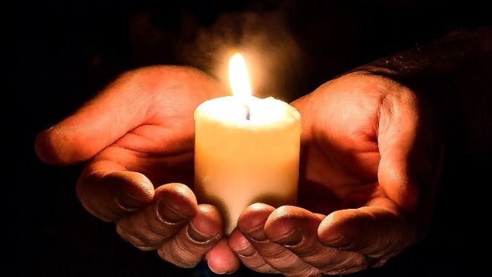 To hænder som en skål med det stearinlys i midten. Helt mørkt rundt om.