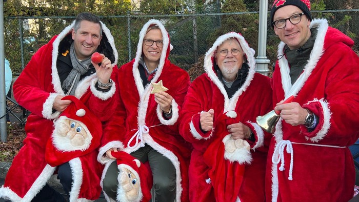 Vier Personen in Weihnachtsmann-Kostümen posieren gemeinsam im Freien