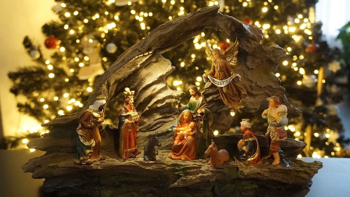 Eine Weihnachtskrippe mit Figuren vor einem beleuchteten Christbaum.